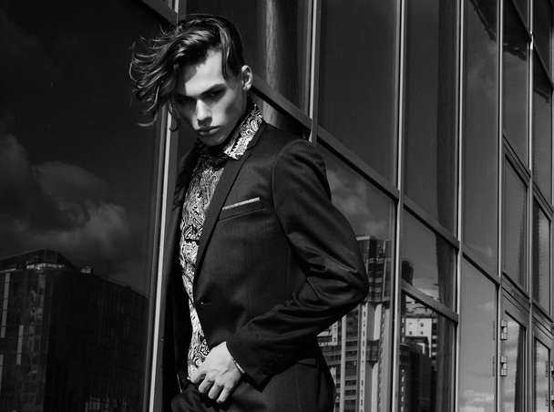 handsome fashion male model dressed in elegant suit posing outdooe. Long haired Metrosexual. Black and white picture. - Foto, afbeelding
