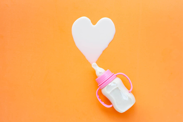 Bottle of milk for baby on orange background. Milk heart shape. - Foto, Imagen