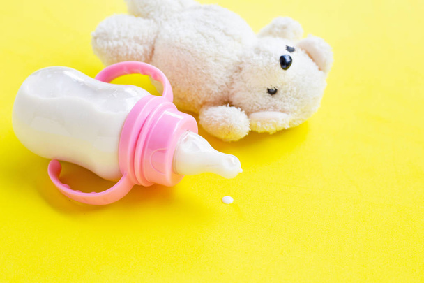 Botella de leche para bebé con juguete oso blanco sobre fondo amarillo
 - Foto, Imagen