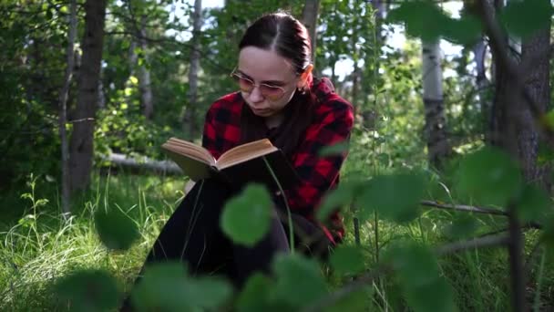Žena čte knihu v zeleném letním lese. - Záběry, video