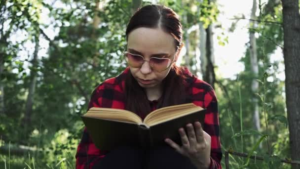 Een vrouw die een boek leest in een groen zomerwoud. - Video