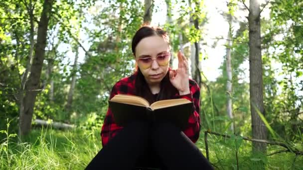 Žena čte knihu v zeleném letním lese. - Záběry, video