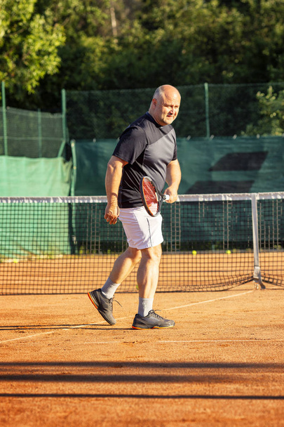 A middle-aged bald man emotionally plays tennis on the court. Loses the opponent. Outdoor. - Fotografie, Obrázek