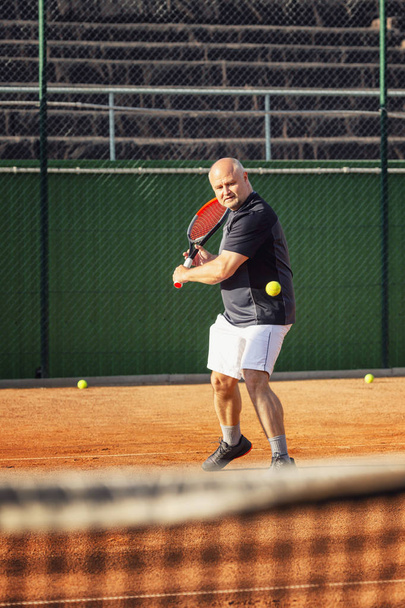 A middle-aged bald man emotionally plays tennis on the court. Outdoor. - Valokuva, kuva