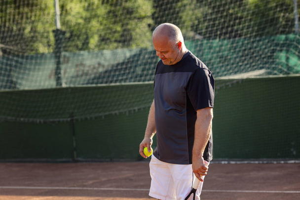 A middle-aged bald man emotionally plays tennis on the court. Loses the opponent. Outdoor. - Фото, зображення