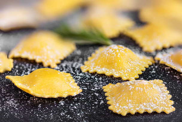 Raviolli with flour and herbs on black background, close up.  It - Foto, afbeelding