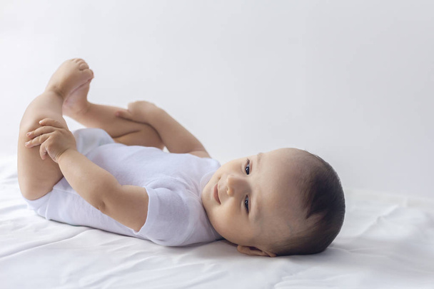 Bebé de 6 meses divirtiéndose en ropa de cama blanca. Lindo bebé acostado en la cama. Familia, nueva vida, concepto de infancia
. - Foto, Imagen