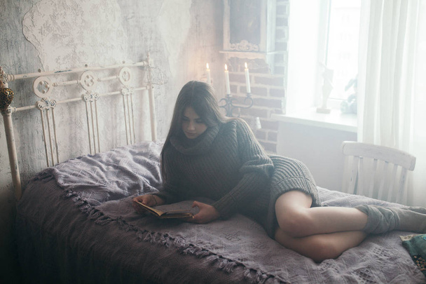 Cozy bed and a beautiful girl, reading a book, concepts of home and comfort - Fotó, kép