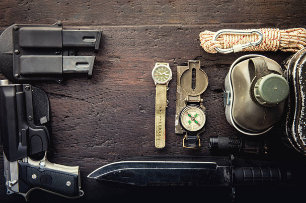 Military tactical equipment for the departure. Assortment of survival hiking gear on wooden background. Top view - vintage film grain filter effect styles - 写真・画像