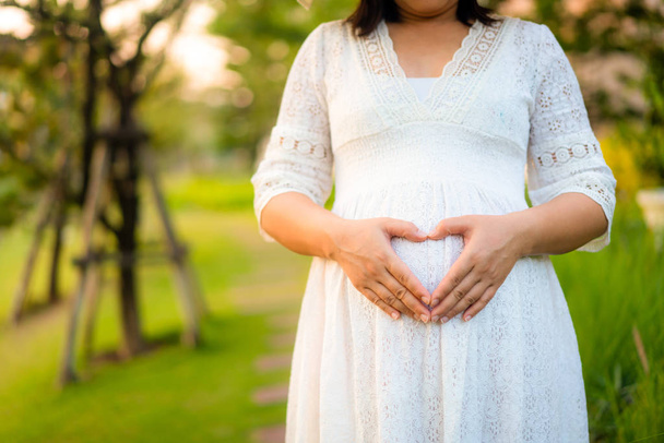 Беременная женщина чувствует себя счастливой в саду дома. - Фото, изображение