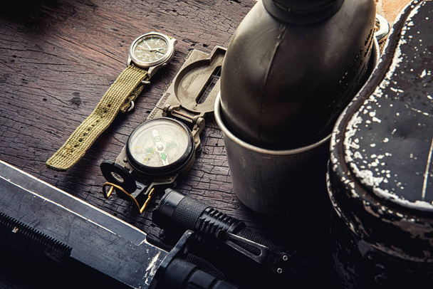 Military tactical equipment for the departure. Assortment of survival hiking gear on wooden background. Top view - vintage film grain filter effect styles - Foto, Bild