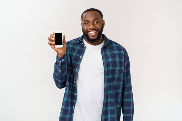 ハンサムなアフリカ系アメリカ人男性は、灰色の背景に孤立し、スマートフォンを提示. - 写真・画像