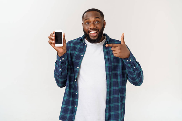 Handsome african american man isolated on grey background, presenting smart phone. - Фото, изображение