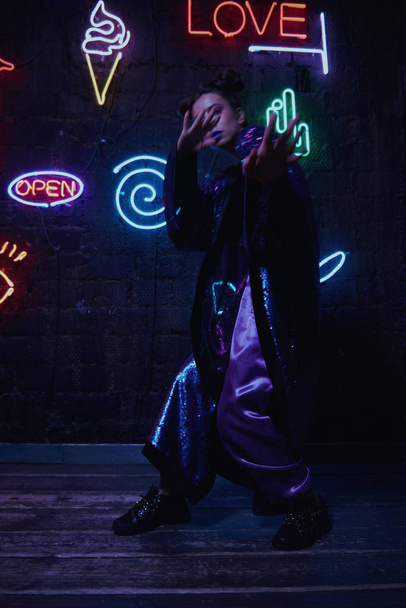 cyberpunk disparo de modelo con albornoz con brillo contra la pared de neón
 - Foto, Imagen