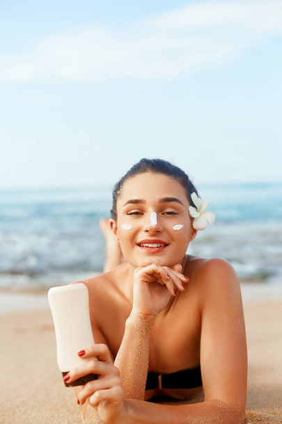 Sunscreen woman applying suntan lotion showing bottle. Beautiful smiling happy woman with suntan cream  lying on beach.  Skin care. Body Sun protection.Sun cream on face. - Valokuva, kuva