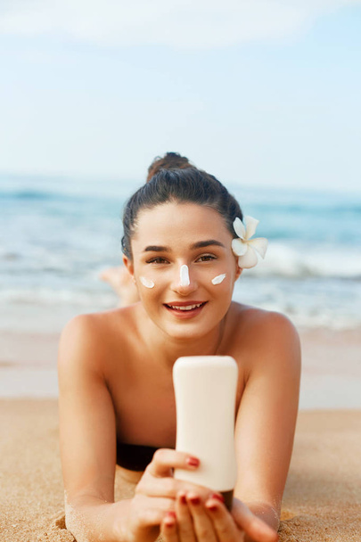 Sunscreen woman applying suntan lotion showing bottle. Beautiful smiling happy woman with suntan cream  lying on beach.  Skin care. Body Sun protection.Sun cream on face. - 写真・画像