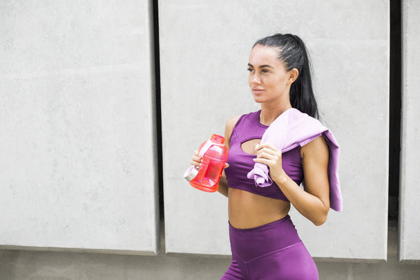 Mooie vrouw runner in stijlvolle kleding houden van een fles met water en rusten na een training. Sport meisje in leggings buiten.  - Foto, afbeelding