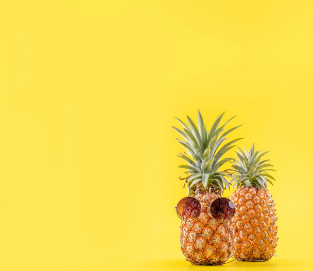 Creative pineapple looking up with sunglasses and shell isolated on yellow background, summer vacation beach idea design pattern, copy space close up - Photo, image