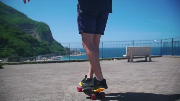 ein Mann, der auf einem Penny Board auf einer Aussichtsplattform Schlittschuh läuft und auf das Meer blickt - Filmmaterial, Video