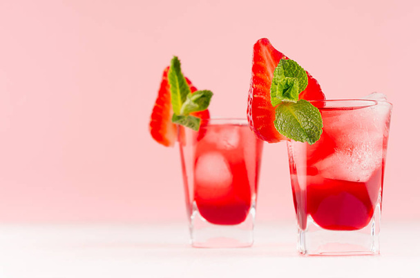 Summer fresh red bright drinks with ice cubes, strawberry slice, green mint on fashion pastel pink color background and white wood table, copy space. - 写真・画像