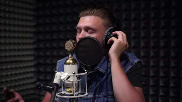 Ένας νέος άνθρωπος τραγουδά σε ένα στούντιο ηχογράφησης σε ένα μικρόφωνο. - Πλάνα, βίντεο