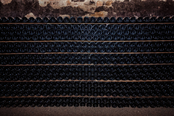 Пляшки червоного вина на дерев'яній полиці. Відпочиваючі пляшки вина, складені на дерев'яних стійках в підвалі
. - Фото, зображення