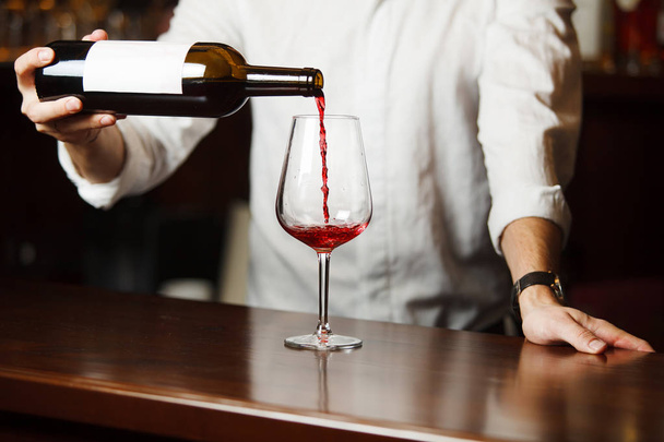 Male sommelier pouring red wine into long-stemmed wineglasses. - Foto, afbeelding