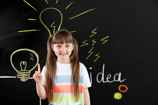 Little girl with raised index finger near drawn light bulbs on dark wall - Photo, Image