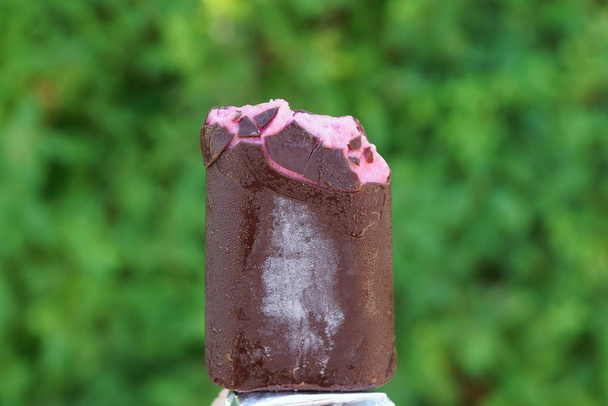  darab hideg rózsaszín fagylaltot barna csokoládéval az utcán egy zöld háttér - Fotó, kép