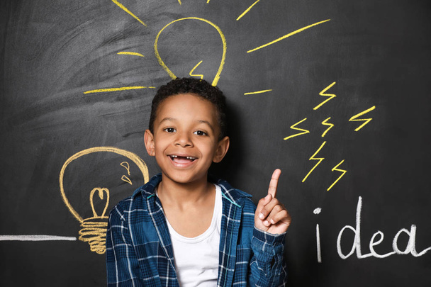 African-American boy with raised index finger near drawn light bulbs on dark wall - Photo, Image