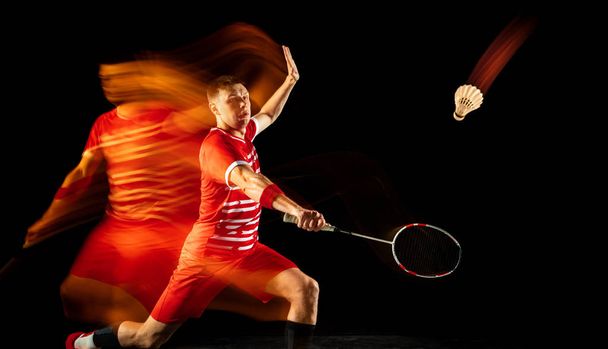 Young man playing badminton isolated on black studio background - Foto, afbeelding