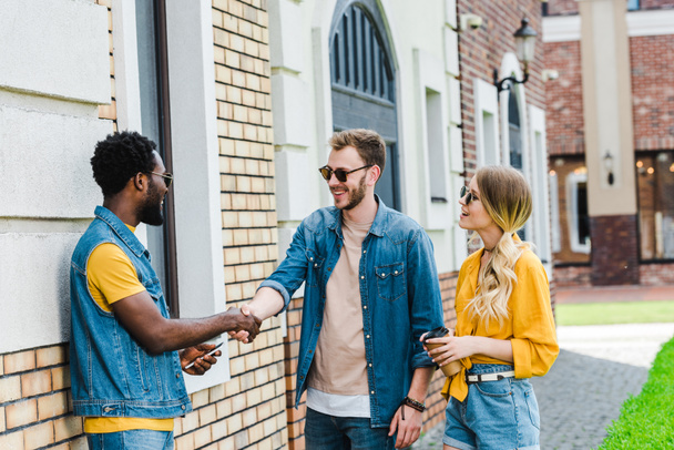 cheerful multicultural men shaking hands near happy woman with paper cup  - Photo, Image