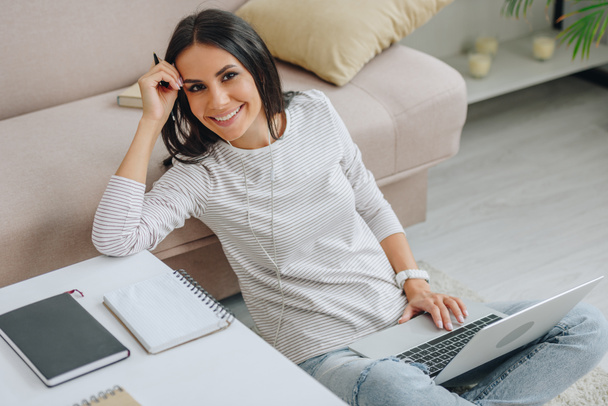 hermosa mujer sentada en el suelo, sonriendo y sosteniendo el ordenador portátil
  - Foto, imagen