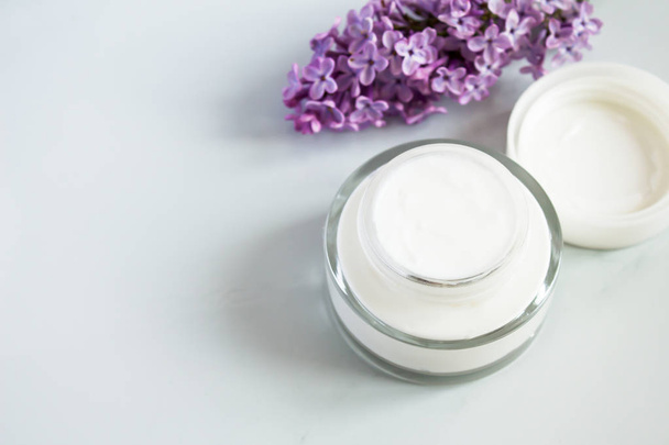 Close-up van Facial moisturizer Cream op witte achtergrond. Detail van glazen pot van bio moisturizer met bloemen. Biologische lotion voor huidverzorgings behandeling. Natuurlijke schoonheid en huidverzorging concept. - Foto, afbeelding