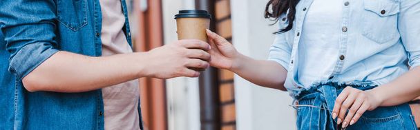 panoramic shot of man giving paper cup to woman while standing outside  - Фото, зображення