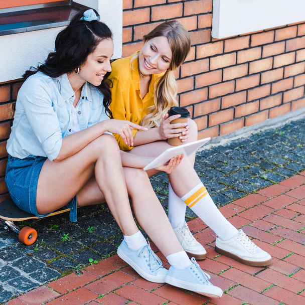 glückliche Frau zeigt mit dem Finger auf digitales Tablet, während sie mit Freund auf dem Penny-Board sitzt  - Foto, Bild