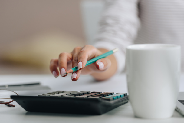 selective focus of woman holding pencil and calculating in apartment  - Photo, Image