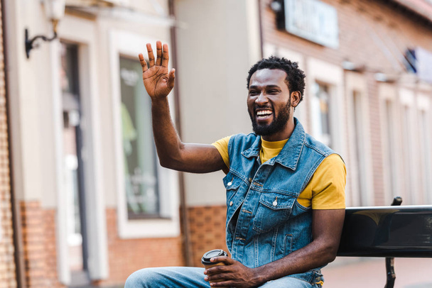 felice uomo africano americano agitando la mano mentre tiene in mano la tazza di carta
  - Foto, immagini