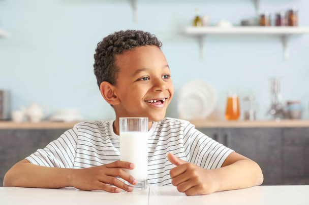 テーブルでミルクのグラスを持つかわいいアフリカ系アメリカ人の少年 - 写真・画像
