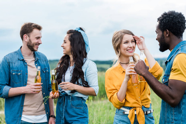 cheerful multicultural men and women holding bottles with beer  - Фото, изображение