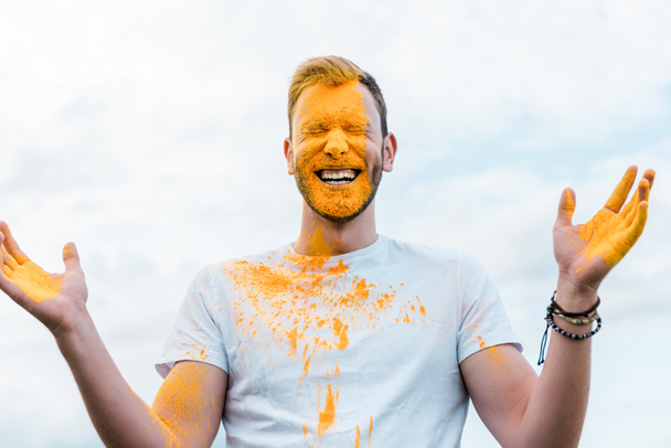 homem feliz com olhos fechados e pintura holi amarelo no rosto
  - Foto, Imagem