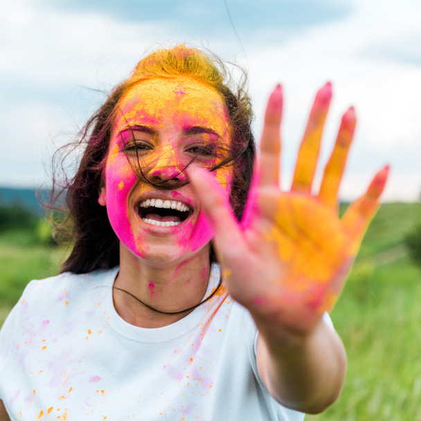 selective focus of cheerful woman with pink and yellow holi paint on face and hands - Photo, image