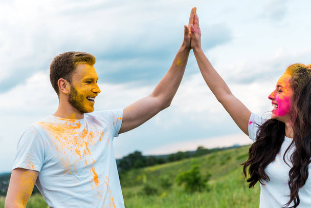  happy man and woman with holi paint on faces giving high five  - Фото, изображение