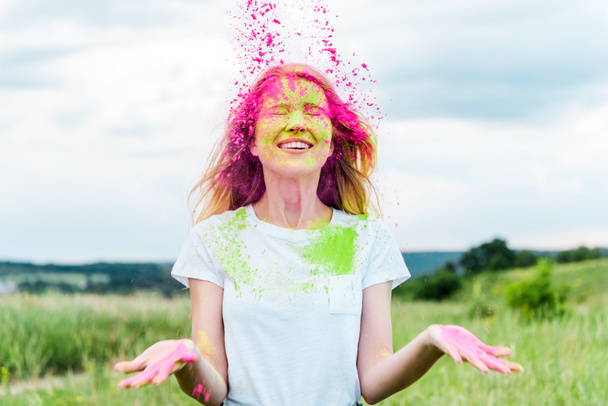 mujer alegre con los ojos cerrados lanzando en el aire pintura holi
  - Foto, Imagen