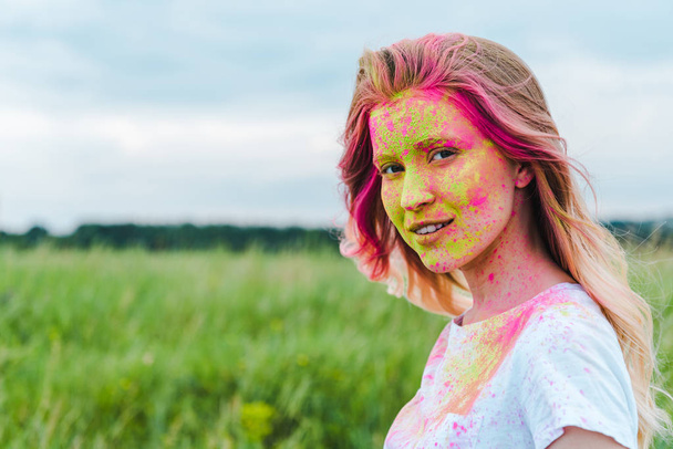  happy young woman with green and pink holi paint on face  - Foto, Imagen