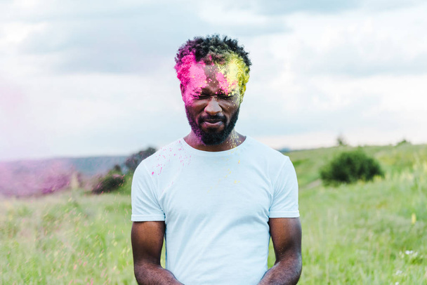uomo afroamericano con gli occhi chiusi in t-shirt bianca e colorate pitture holi sul viso
 - Foto, immagini