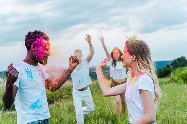 selective focus of multicultural friends with colorful holi paints on faces - Valokuva, kuva