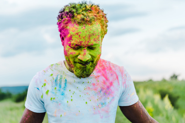 ευτυχισμένος Αφρικανός Αμερικανός άνθρωπος με πολύχρωμα Holi ζωγραφίζει στο πρόσωπο - Φωτογραφία, εικόνα