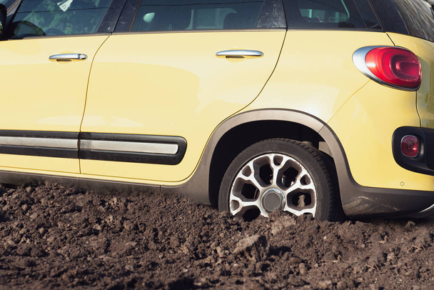 Amarillo coche SUV moderno atascado en el barro en el día soleado. Vista lateral. Fotografía conceptual fuera de la carretera. Coche roto
. - Foto, imagen