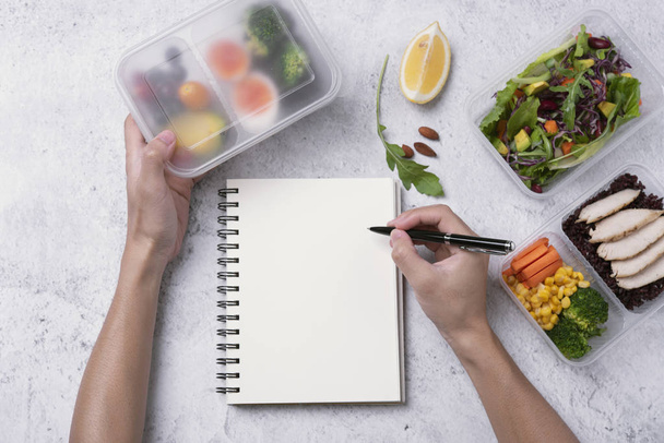 χέρια κρατώντας ένα υγιεινό κουτί μεσημεριανού γεύματος και ένα κενό σημειωματάριο για το κείμενό σας - Φωτογραφία, εικόνα